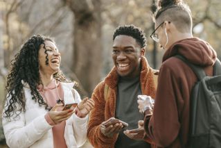 Three friends sharing a joyful moment, laughing together outdoors in a park setting.